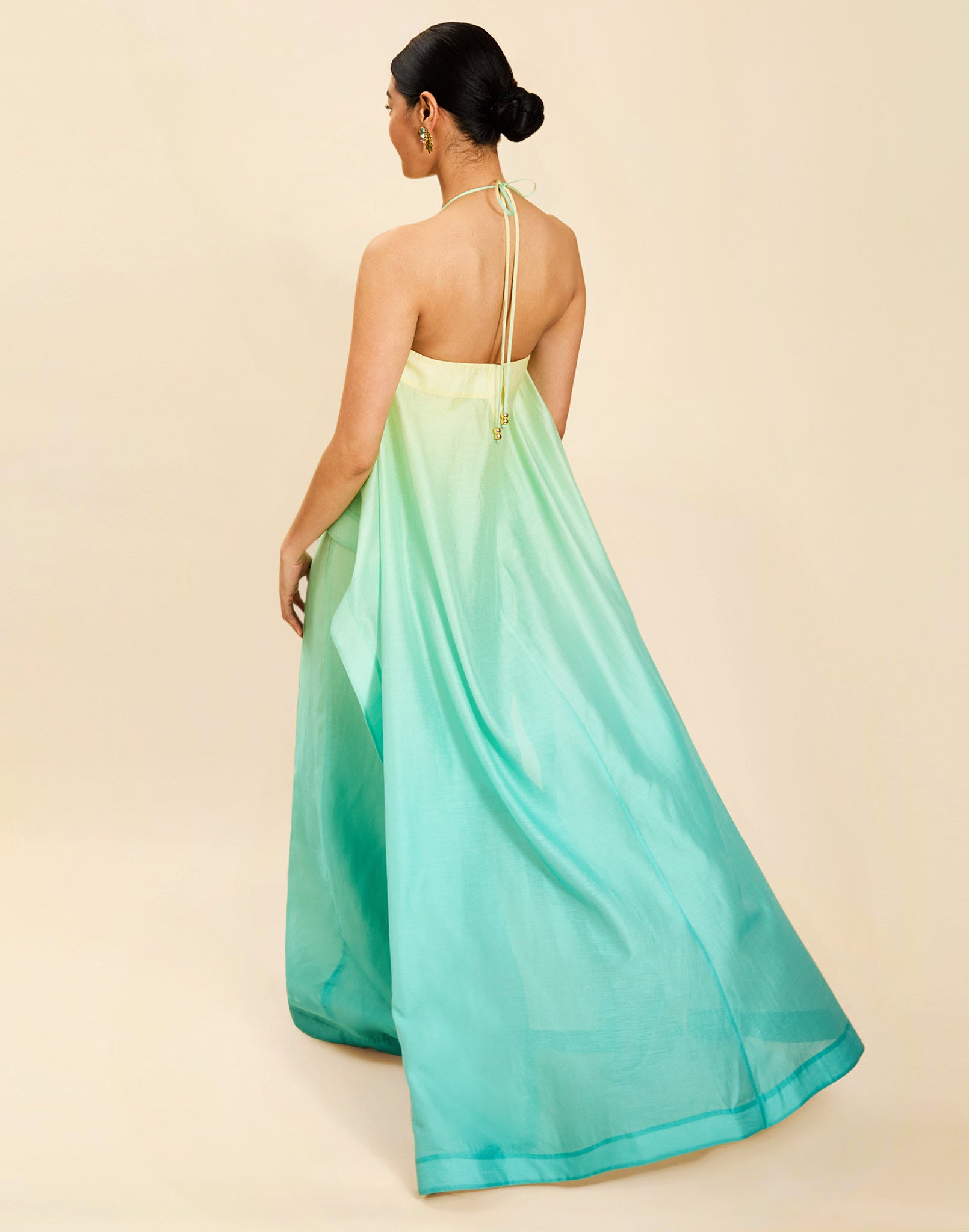 Woman wearing the Mestiza Mariposa Convertible Gown in Tuscan Sunrise print, featuring a column silhouette, removable cape overlay, racerback neckline, open back, self-tie halter straps, and linen organza fabrication.