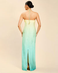 Woman wearing the Mestiza Mariposa Convertible Gown in Tuscan Sunrise print, featuring a column silhouette, removable cape overlay, racerback neckline, open back, self-tie halter straps, and linen organza fabrication.