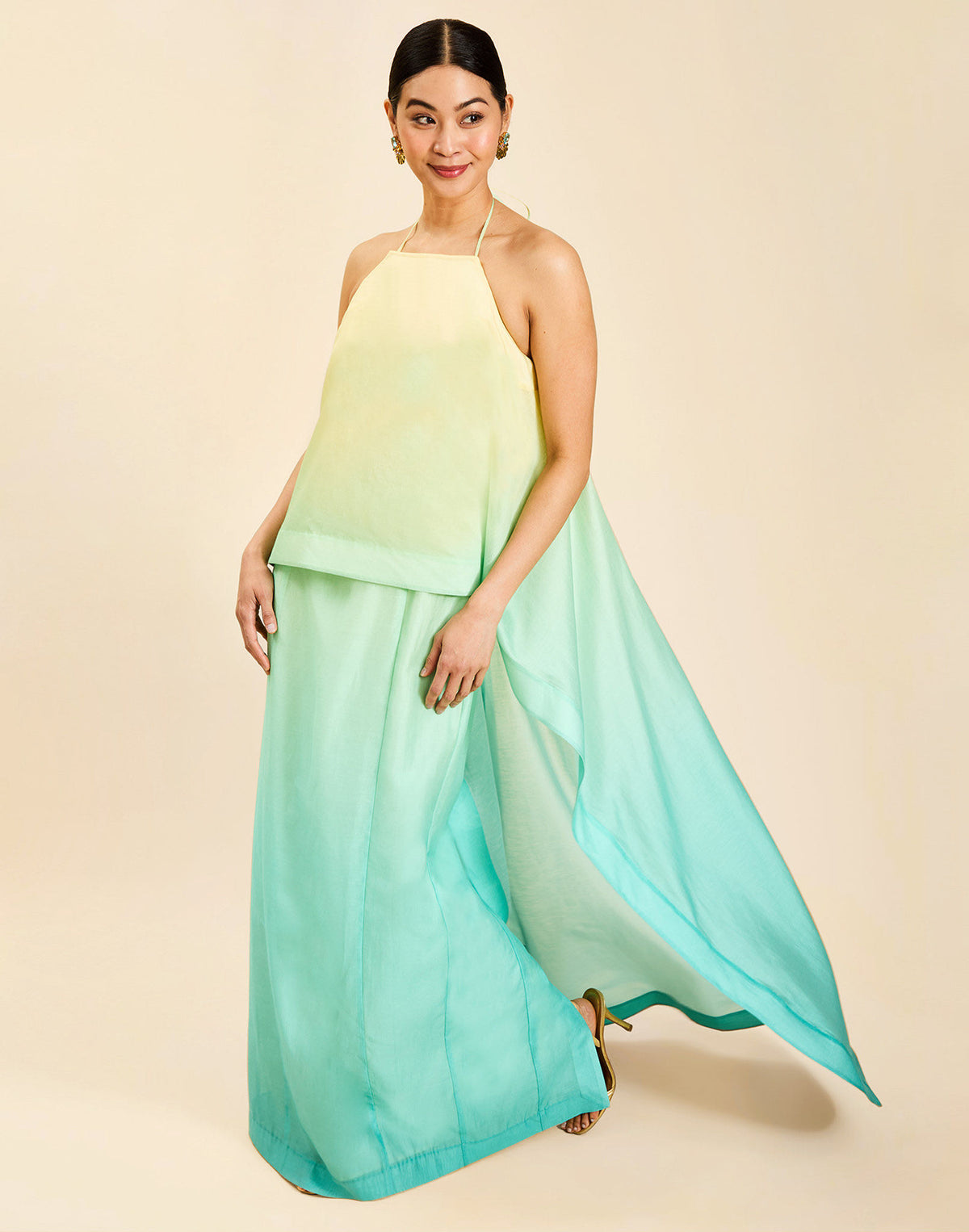 Woman wearing the Mestiza Mariposa Convertible Gown in Tuscan Sunrise print, featuring a column silhouette, removable cape overlay, racerback neckline, open back, self-tie halter straps, and linen organza fabrication.