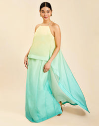 Woman wearing the Mestiza Mariposa Convertible Gown in Tuscan Sunrise print, featuring a column silhouette, removable cape overlay, racerback neckline, open back, self-tie halter straps, and linen organza fabrication.