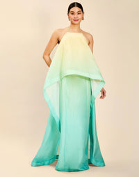 Woman wearing the Mestiza Mariposa Convertible Gown in Tuscan Sunrise print, featuring a column silhouette, removable cape overlay, racerback neckline, open back, self-tie halter straps, and linen organza fabrication.