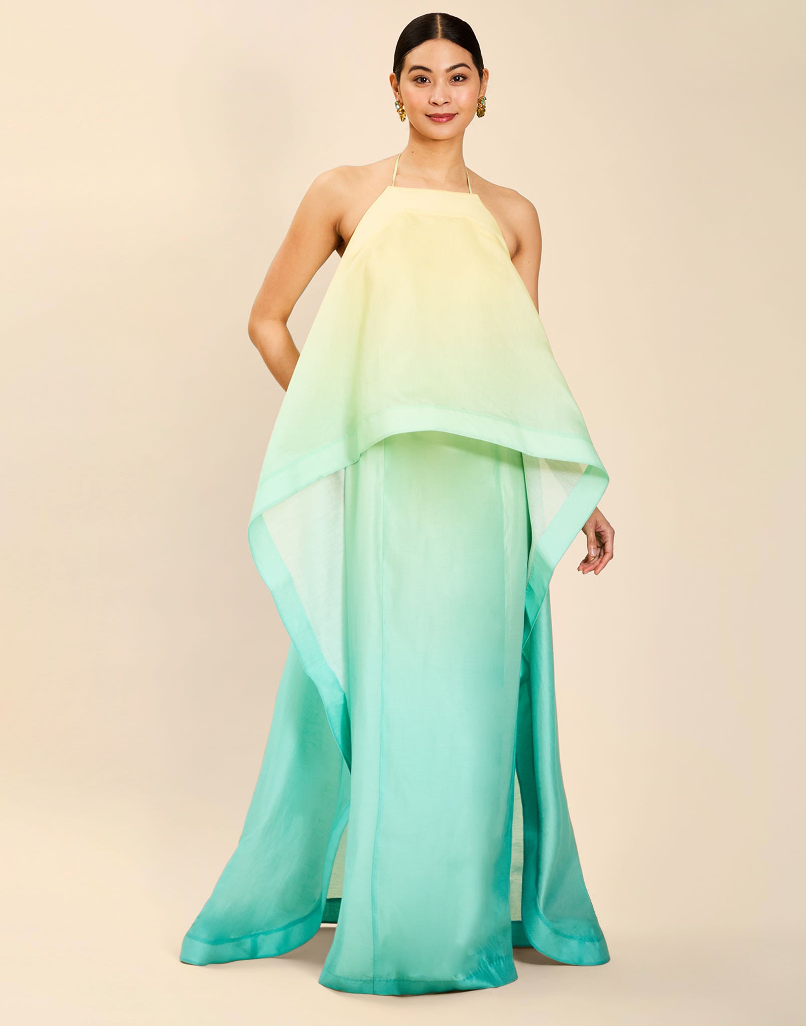Woman wearing the Mestiza Mariposa Convertible Gown in Tuscan Sunrise print, featuring a column silhouette, removable cape overlay, racerback neckline, open back, self-tie halter straps, and linen organza fabrication.