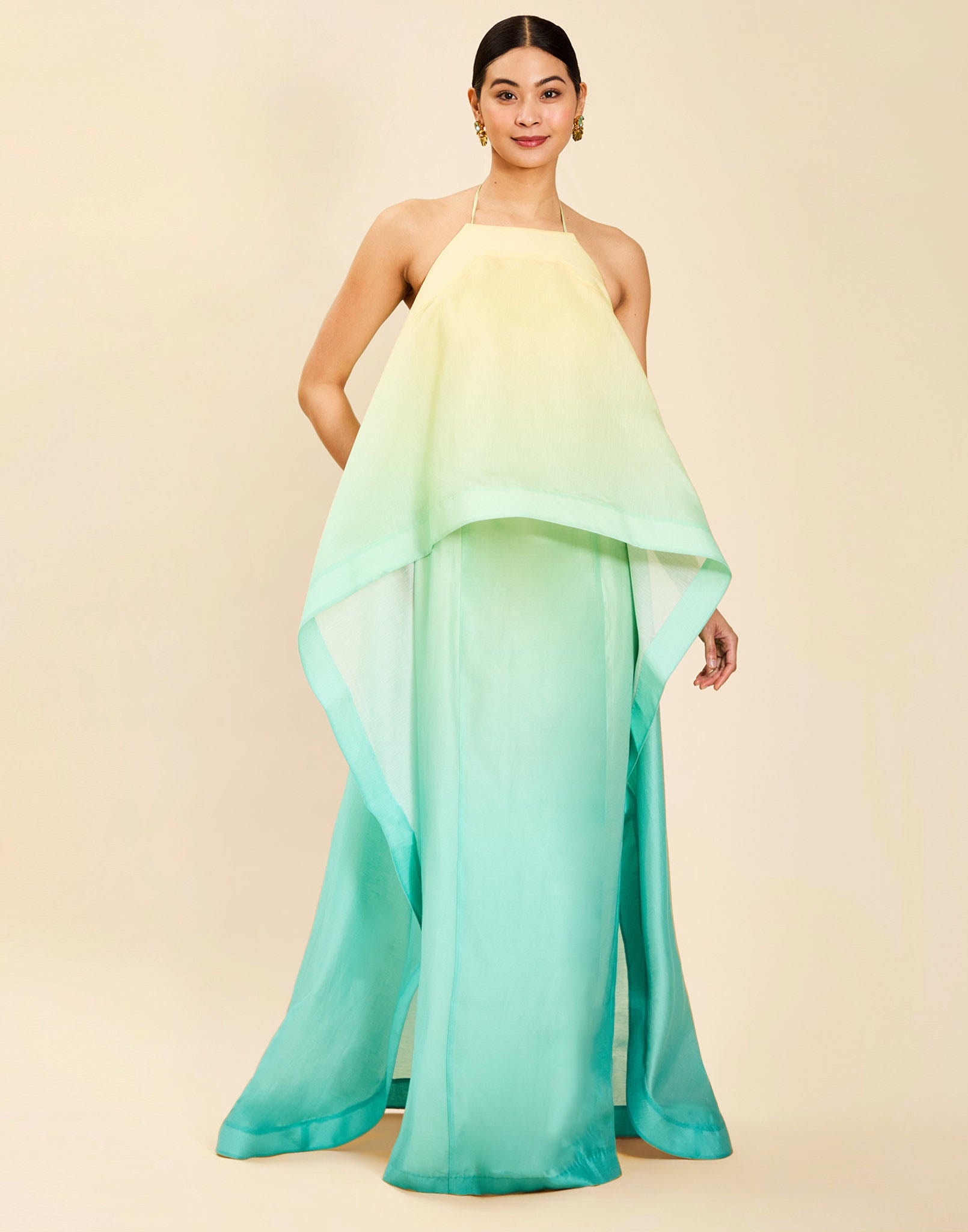 Woman wearing the Mestiza Mariposa Convertible Gown in Tuscan Sunrise print, featuring a column silhouette, removable cape overlay, racerback neckline, open back, self-tie halter straps, and linen organza fabrication.