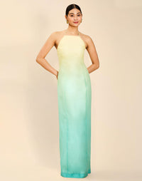 Woman wearing the Mestiza Mariposa Convertible Gown in Tuscan Sunrise print, featuring a column silhouette, removable cape overlay, racerback neckline, open back, self-tie halter straps, and linen organza fabrication.