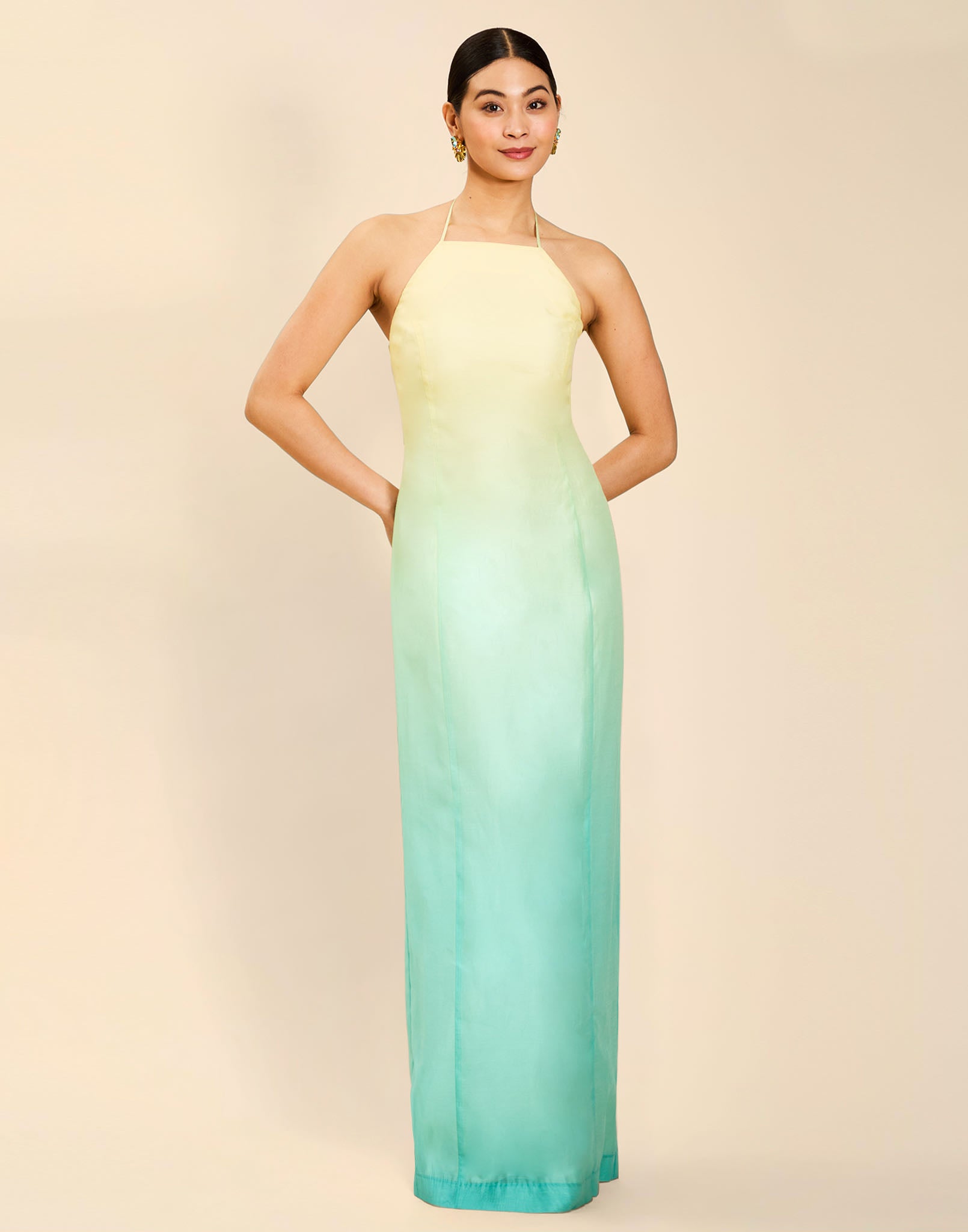 Woman wearing the Mestiza Mariposa Convertible Gown in Tuscan Sunrise print, featuring a column silhouette, removable cape overlay, racerback neckline, open back, self-tie halter straps, and linen organza fabrication.
