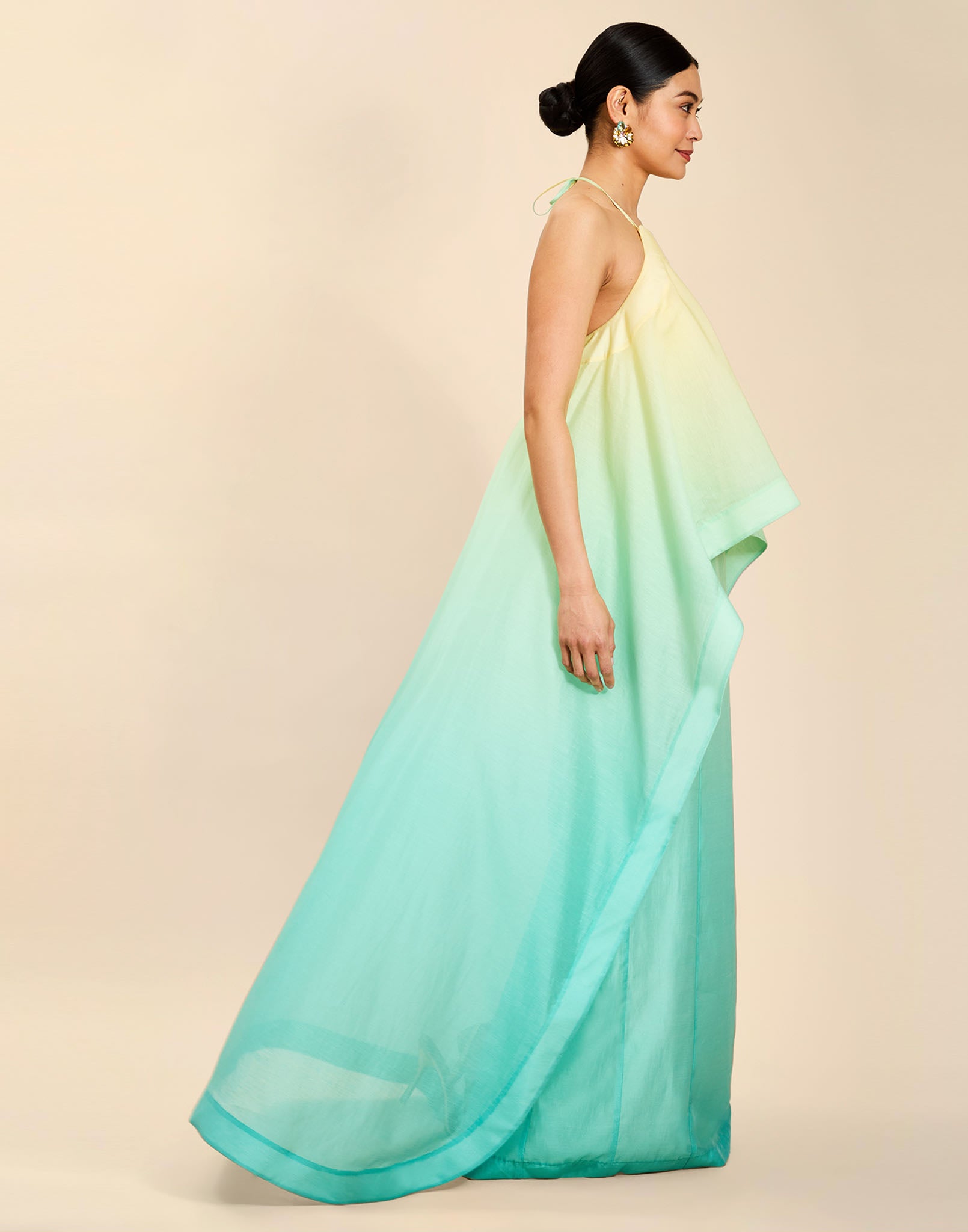 Woman wearing the Mestiza Mariposa Convertible Gown in Tuscan Sunrise print, featuring a column silhouette, removable cape overlay, racerback neckline, open back, self-tie halter straps, and linen organza fabrication.