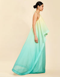 Woman wearing the Mestiza Mariposa Convertible Gown in Tuscan Sunrise print, featuring a column silhouette, removable cape overlay, racerback neckline, open back, self-tie halter straps, and linen organza fabrication.