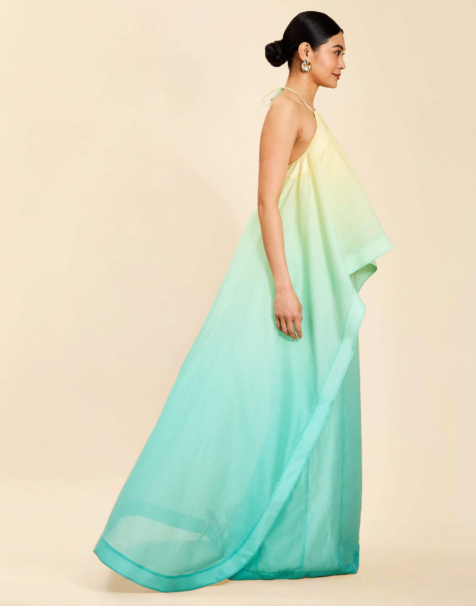 Woman wearing the Mestiza Mariposa Convertible Gown in Tuscan Sunrise print, featuring a column silhouette, removable cape overlay, racerback neckline, open back, self-tie halter straps, and linen organza fabrication.