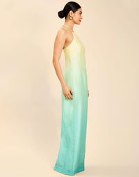 Woman wearing the Mestiza Mariposa Convertible Gown in Tuscan Sunrise print, featuring a column silhouette, removable cape overlay, racerback neckline, open back, self-tie halter straps, and linen organza fabrication.