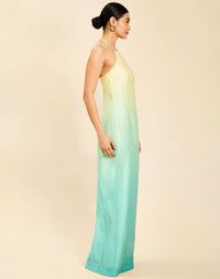 Woman wearing the Mestiza Mariposa Convertible Gown in Tuscan Sunrise print, featuring a column silhouette, removable cape overlay, racerback neckline, open back, self-tie halter straps, and linen organza fabrication.