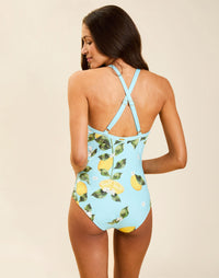Model wearing Nemi Halter One Piece in Sorrento Citrus with cross-front straps, bow detail, and contrast-trim neckline.