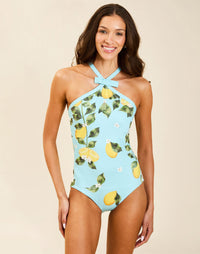 Model wearing Nemi Halter One Piece in Sorrento Citrus with cross-front straps, bow detail, and contrast-trim neckline.