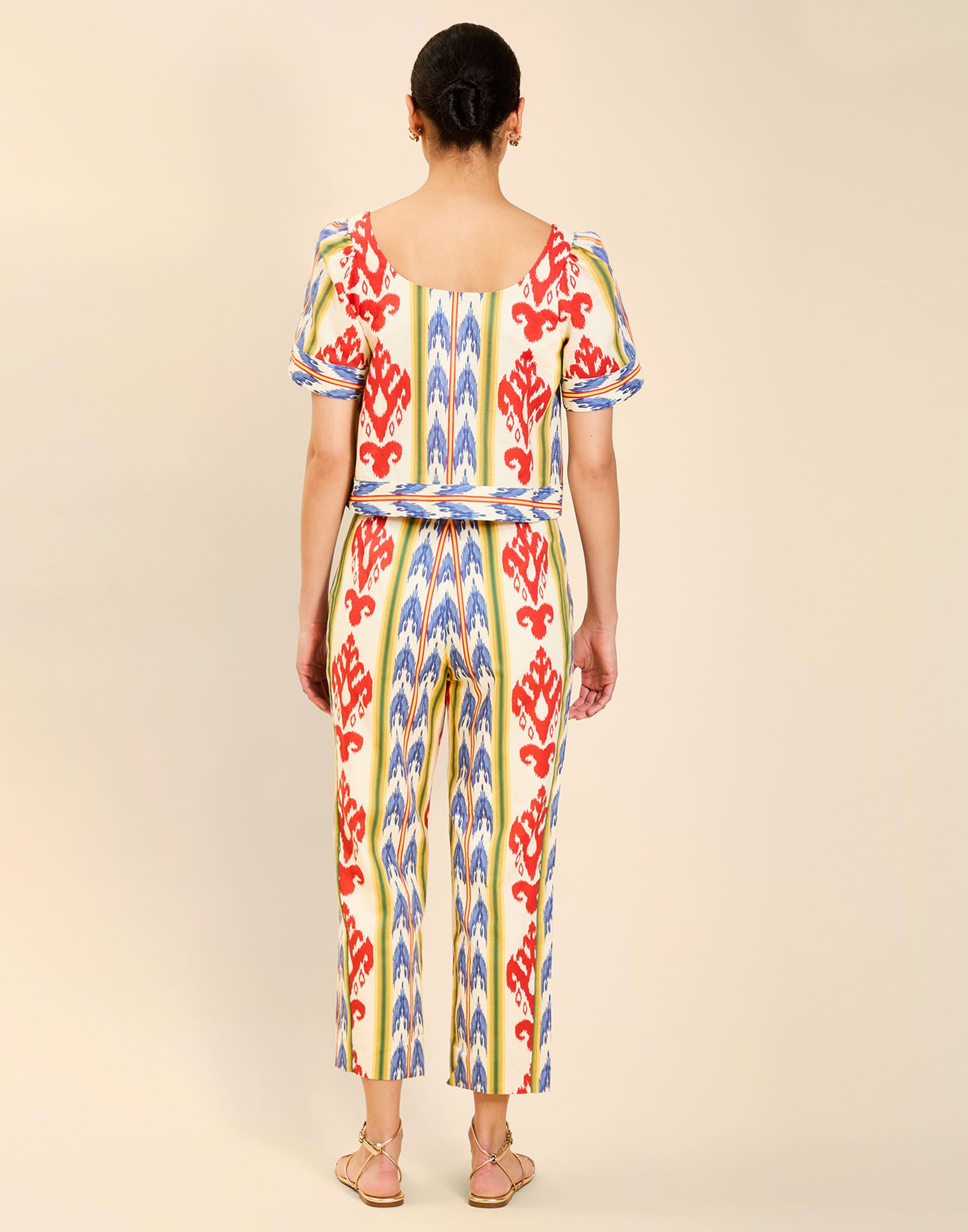 Woman wearing the Mestiza Palau Cigarette Pant in Ikat Sunrise print, featuring a slim-fit cigarette silhouette, front pleat detailing, cropped ankle-length fit, and lightweight linen fabrication.