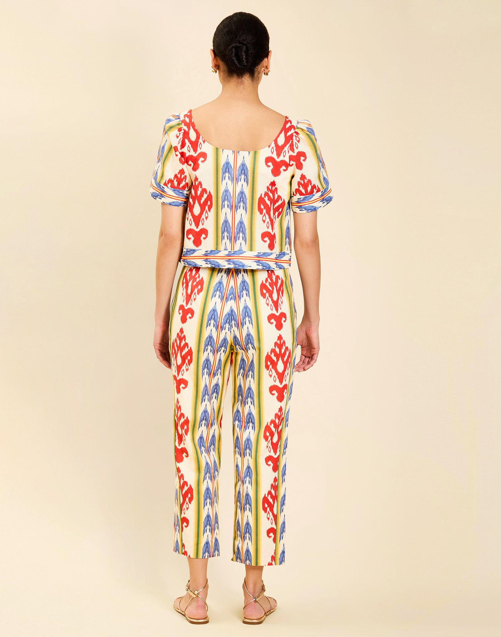 Woman wearing the Mestiza Palau Cigarette Pant in Ikat Sunrise print, featuring a slim-fit cigarette silhouette, front pleat detailing, cropped ankle-length fit, and lightweight linen fabrication.