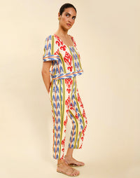 Woman wearing the Mestiza Palau Cigarette Pant in Ikat Sunrise print, featuring a slim-fit cigarette silhouette, front pleat detailing, cropped ankle-length fit, and lightweight linen fabrication.