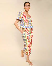 Woman wearing the Mestiza Palau Cigarette Pant in Ikat Sunrise print, featuring a slim-fit cigarette silhouette, front pleat detailing, cropped ankle-length fit, and lightweight linen fabrication.