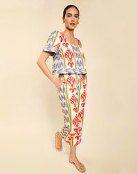 Woman wearing the Mestiza Palau Cigarette Pant in Ikat Sunrise print, featuring a slim-fit cigarette silhouette, front pleat detailing, cropped ankle-length fit, and lightweight linen fabrication.