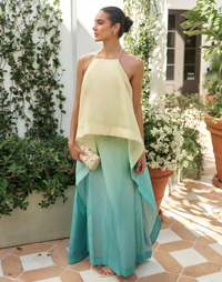 Woman wearing the Mestiza Mariposa Convertible Gown in Tuscan Sunrise print, featuring a column silhouette, removable cape overlay, racerback neckline, open back, self-tie halter straps, and linen organza fabrication.