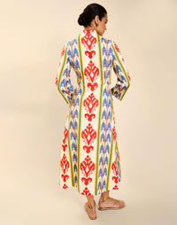 Woman wearing the Mestiza Shoshi Midi Dress in Ikat Sunrise print, featuring a fitted bodice, A-line midi skirt, mandarin collar, functional frog tie closures, side seam pockets, and linen fabrication.