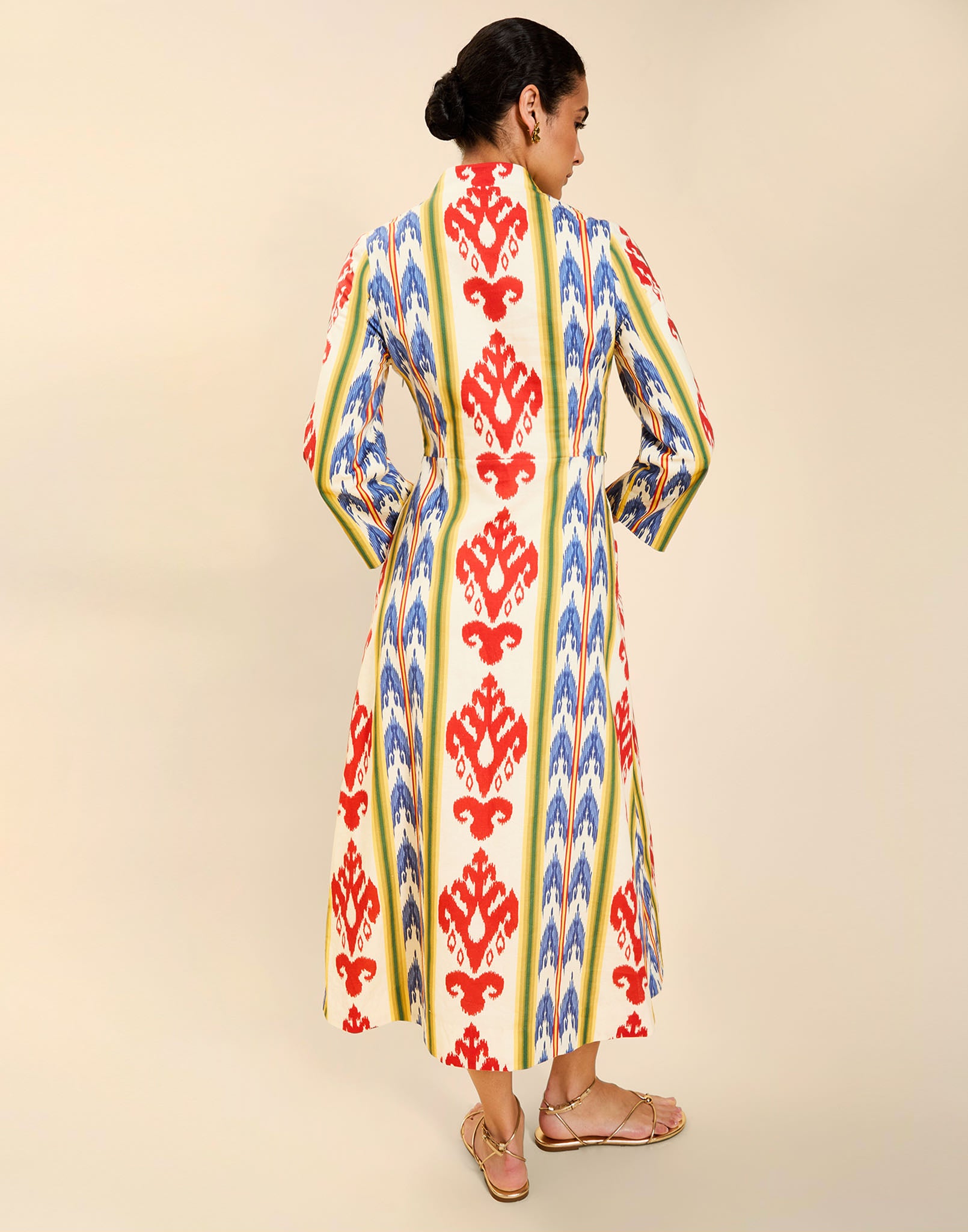 Woman wearing the Mestiza Shoshi Midi Dress in Ikat Sunrise print, featuring a fitted bodice, A-line midi skirt, mandarin collar, functional frog tie closures, side seam pockets, and linen fabrication.