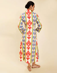 Woman wearing the Mestiza Shoshi Midi Dress in Ikat Sunrise print, featuring a fitted bodice, A-line midi skirt, mandarin collar, functional frog tie closures, side seam pockets, and linen fabrication.