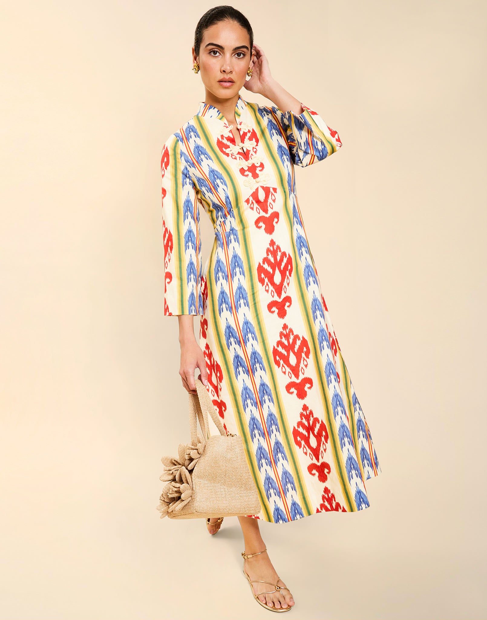 Woman wearing the Mestiza Shoshi Midi Dress in Ikat Sunrise print, featuring a fitted bodice, A-line midi skirt, mandarin collar, functional frog tie closures, side seam pockets, and linen fabrication.