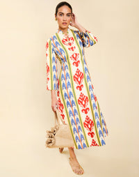 Woman wearing the Mestiza Shoshi Midi Dress in Ikat Sunrise print, featuring a fitted bodice, A-line midi skirt, mandarin collar, functional frog tie closures, side seam pockets, and linen fabrication.
