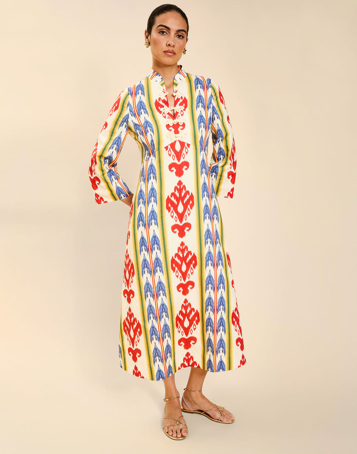 Woman wearing the Mestiza Shoshi Midi Dress in Ikat Sunrise print, featuring a fitted bodice, A-line midi skirt, mandarin collar, functional frog tie closures, side seam pockets, and linen fabrication.