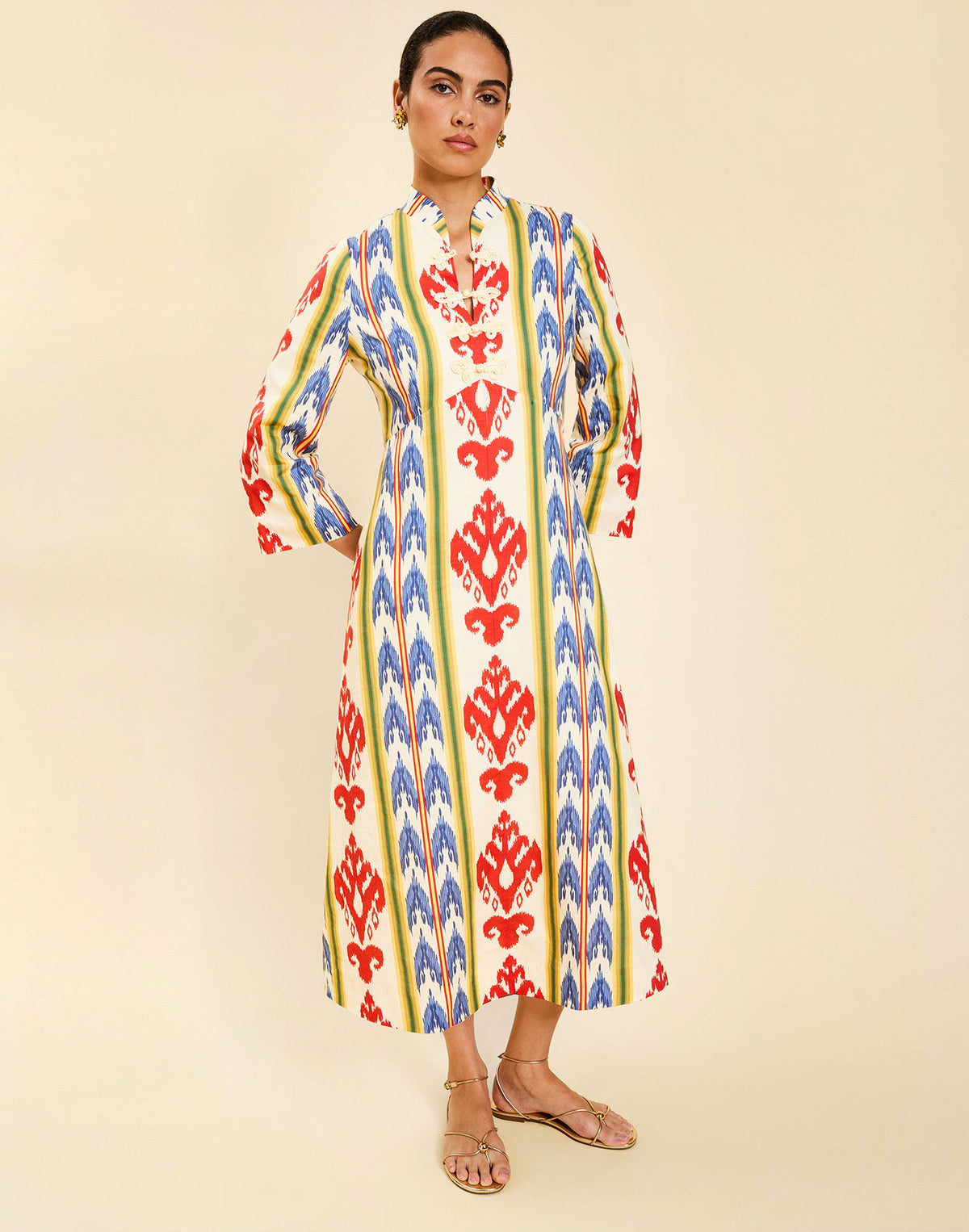 Woman wearing the Mestiza Shoshi Midi Dress in Ikat Sunrise print, featuring a fitted bodice, A-line midi skirt, mandarin collar, functional frog tie closures, side seam pockets, and linen fabrication.