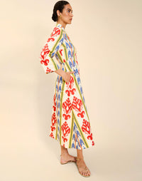 Woman wearing the Mestiza Shoshi Midi Dress in Ikat Sunrise print, featuring a fitted bodice, A-line midi skirt, mandarin collar, functional frog tie closures, side seam pockets, and linen fabrication.