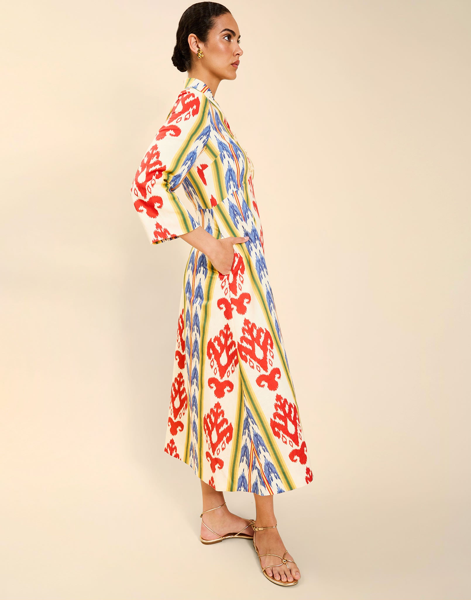 Woman wearing the Mestiza Shoshi Midi Dress in Ikat Sunrise print, featuring a fitted bodice, A-line midi skirt, mandarin collar, functional frog tie closures, side seam pockets, and linen fabrication.