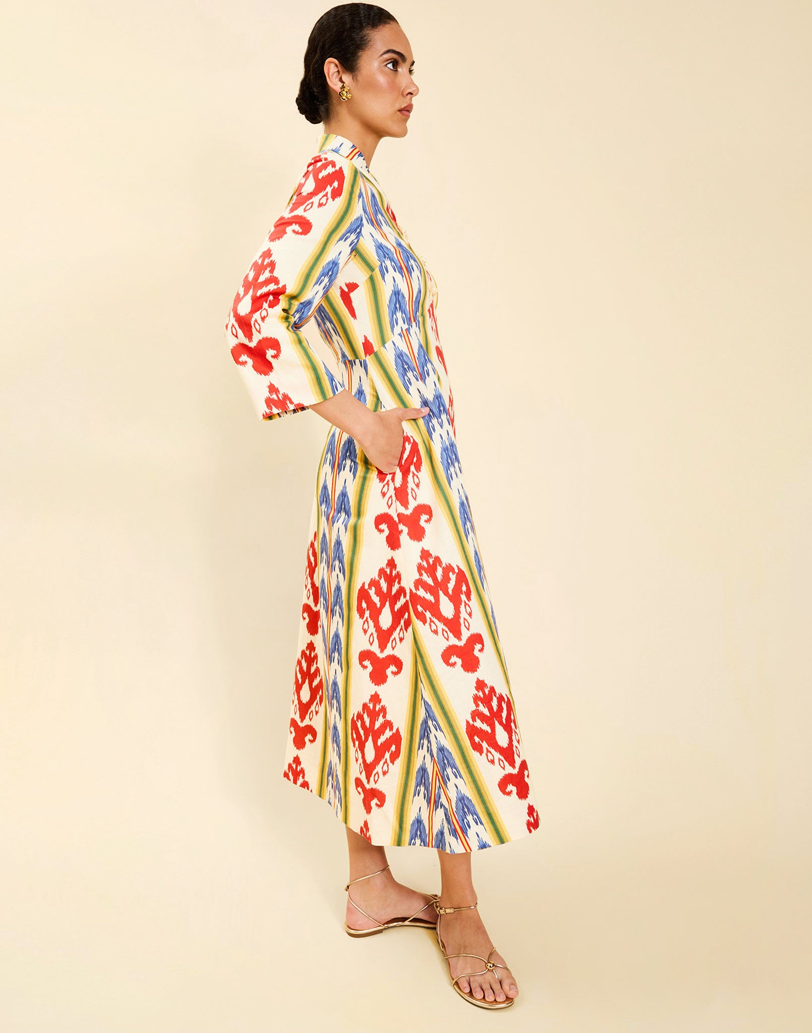 Woman wearing the Mestiza Shoshi Midi Dress in Ikat Sunrise print, featuring a fitted bodice, A-line midi skirt, mandarin collar, functional frog tie closures, side seam pockets, and linen fabrication.