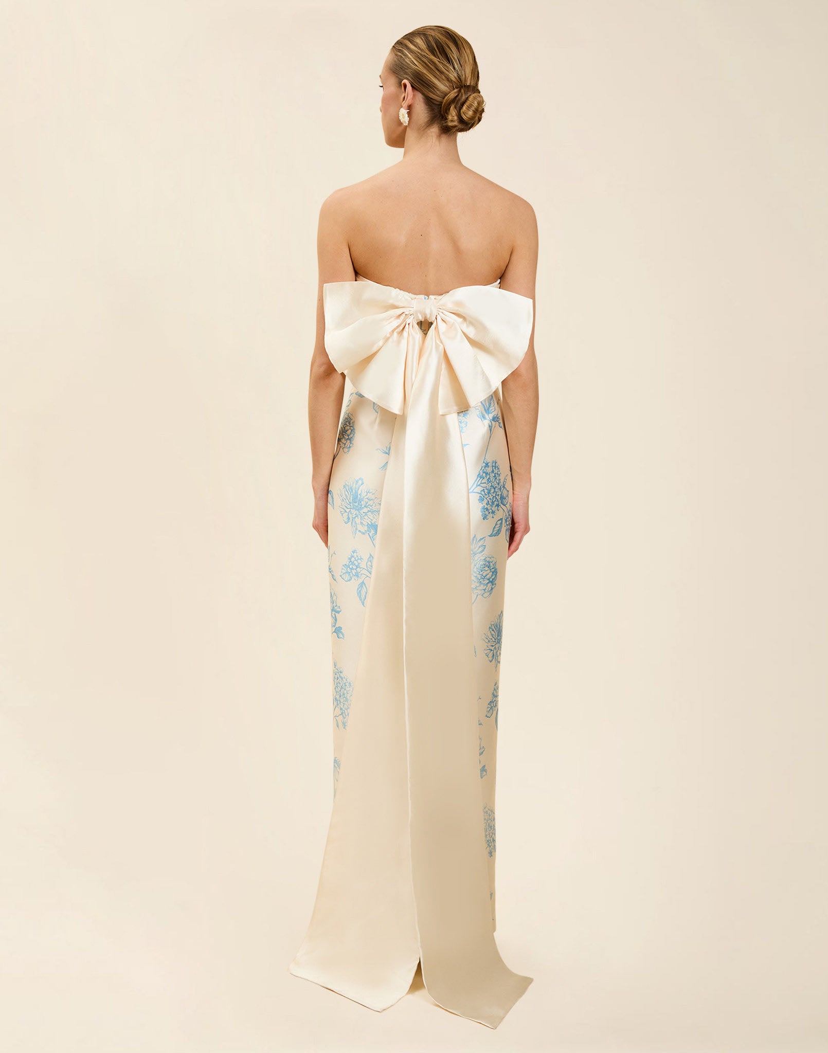 Solstice Gown in Powder Batiste poly silk twill with strapless neckline, removable pleated band, statement bow detail, and fitted gown silhouette.
