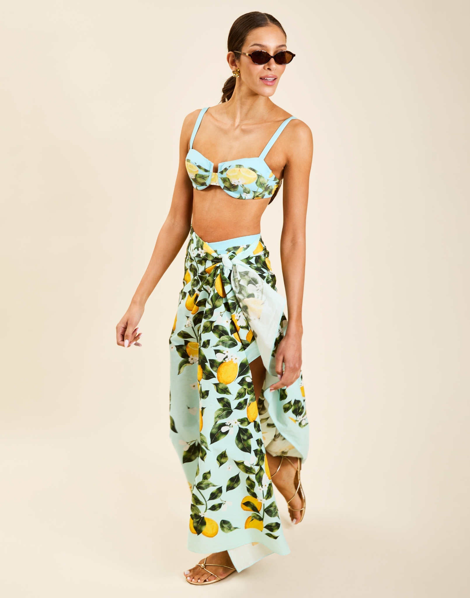Model wearing Isla Sarong in Sorrento Citrus cotton poplin with contrast border tied at waist over swimwear.
