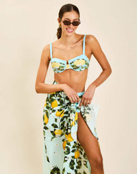 Model wearing Isla Sarong in Sorrento Citrus cotton poplin with contrast border tied at waist over swimwear.