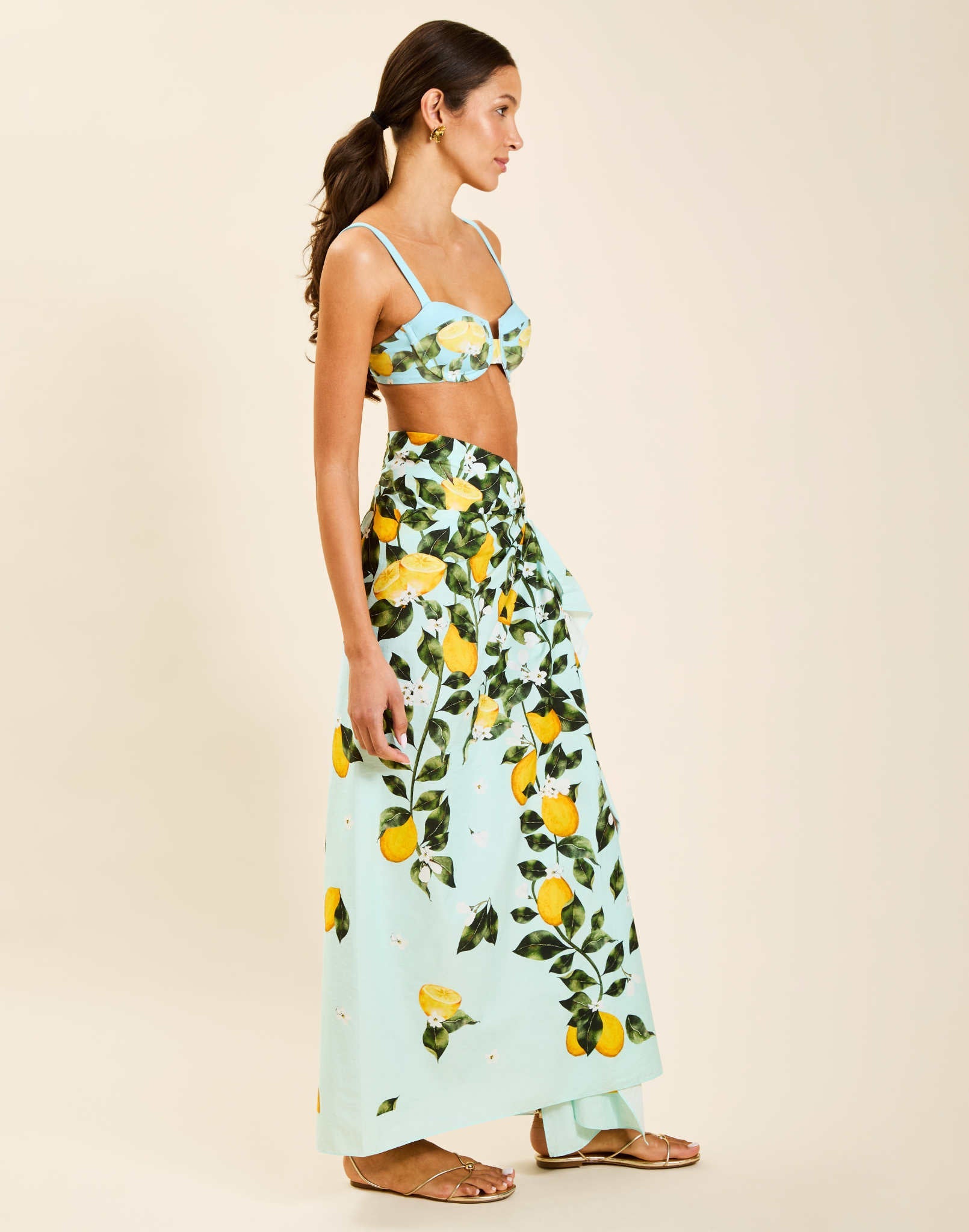 Model wearing Isla Sarong in Sorrento Citrus cotton poplin with contrast border tied at waist over swimwear.